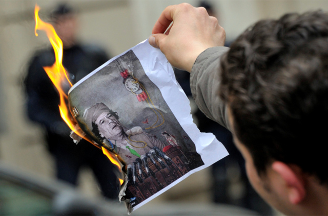 Un hombre quema una imagen de Gadafi en el Consulado de Libia en París. | Reuters