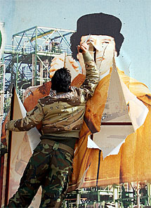 Un rebelde libio rompe una valla publicitaria con la imagen de Gadafi en Ras Lanu. | Efe
