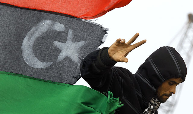 Un rebelde hace el signo de la victoria ante una bandera libia en Ben Jawad. | Reuters