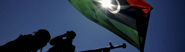 Rebendes libios revisan su armamento frente a la bandera pre-Gadafi, en Brega. | EFE