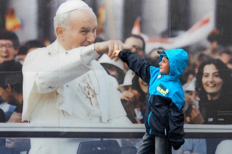 Un chico posa de forma bromista ante un cartel de Juan Pablo II en Cracovia. | Reuters