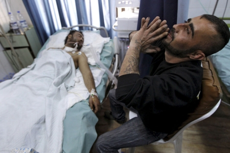 Un hombre reza al lado de su hermano herido en los enfrentamientos.| Hussein Malla/AP