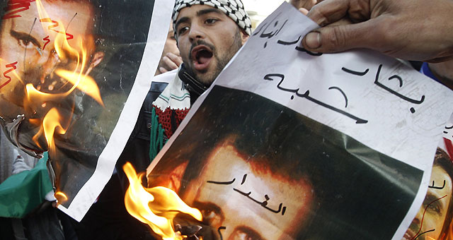 Dos manifestantes queman retratos del presidente sirio, Bashar al Assad. | Reuters