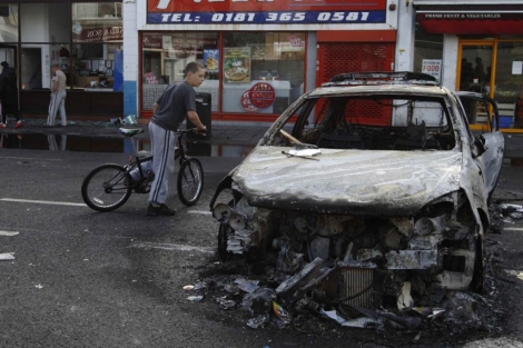 Un nio observa los restos de un coche calcinado en los disturbios. | Reuters