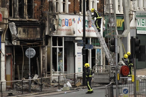 Los bomberos limpian un barrio londinense este martes. | AP