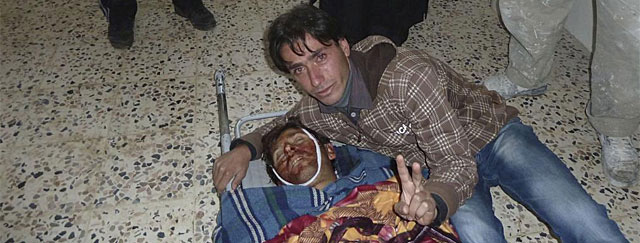 Un sirio hace el smbolo de la victoria junto a un familiar fallecido cerca de Homs. | Reuters
