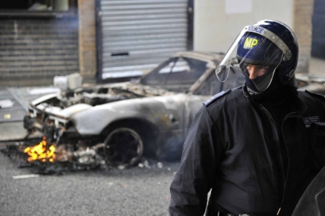 Un polica frente a un coche incendiado en Hackney. | Toby Melville, Reuters