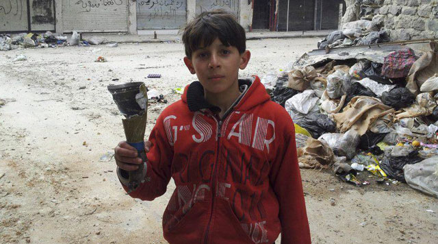 Un niño muestra los restos de un proyectil en un barrio de Homs (Siria). | Reuters