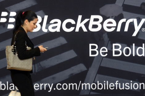 Una mujer pasa frente a un anuncio de Blackberry mientras usa un mvil de la marca. | Reuters