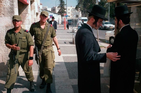 Soldados israeles, que patrullan Jerusalen, pasan junto a dos judios ultraortodoxos.