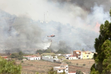Un helicptero trata de evitar que las llamas alcancen a unas viviendas de Erjos en el municipio de El Tanque. | Efe