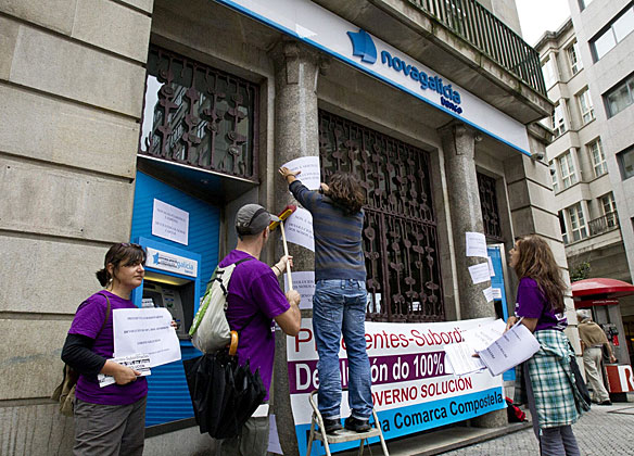 Miembros de la plataforma de afectados por las preferentes pegan carteles en una sucursal de Novagalicia Banco. | Efe