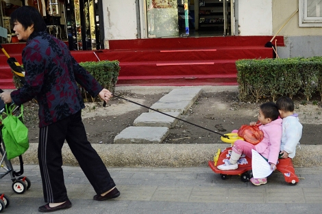 Una mujer arrastra un carrito con dos nios en Pekn. | Afp