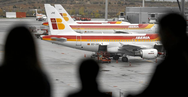 Unos pasajeros observan en Barajas varios aviones de Iberia. | Reuters