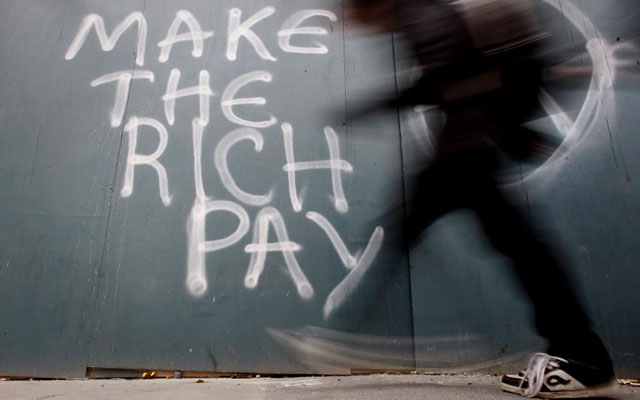 Una hombre pasa en Dubln junto a una pintada que reza 'Que paguen los ricos'. | E.M.