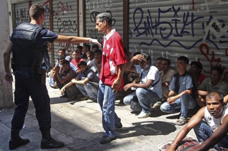Un polica griego mantiene retenidos a unos inmigrantes residentes en Atenas. | Efe