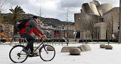 Un hombre pasea en bici por un parque nevado en Bilbao, este lunes. | Efe