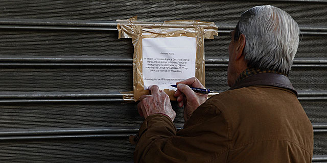 Un hombre escribe 'deshonra' en el cartel de un banco que anuncia que no abrir. | Efe