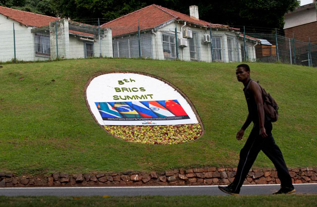 Un hombre camina en frente de un cartel floral que anuncia la celebración de la cumbre. | Reuters