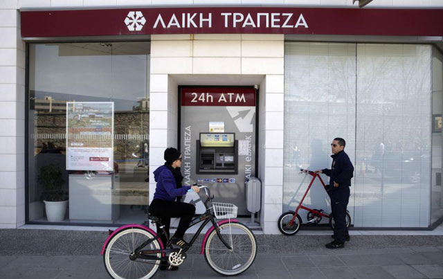 Ciclistas pasan frente a una oficina de Laiki Bank en Nicosia. |Afp