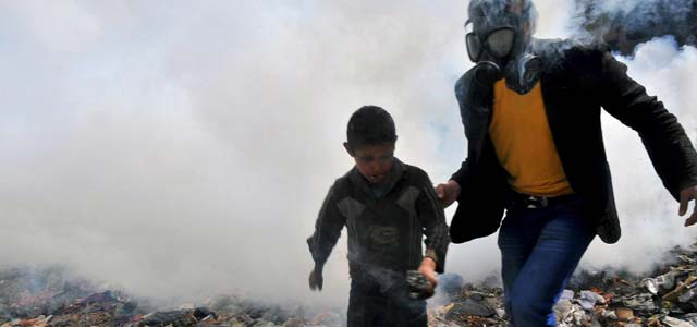 Un hombre con máscara de gas ayuda a un niño a huir del humo en Alepo. | Afp