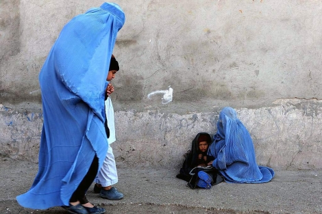 Una mujer con burka pasea frente a otra que pide limosna en Kabul. | Afp