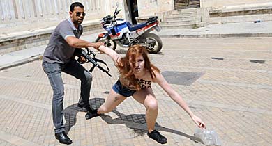Un polica armado detiene a una de las activistas semidesnudas en Tnez. | Afp