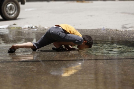 Un niño bebe agua de un charco en Alepo.| Reuters