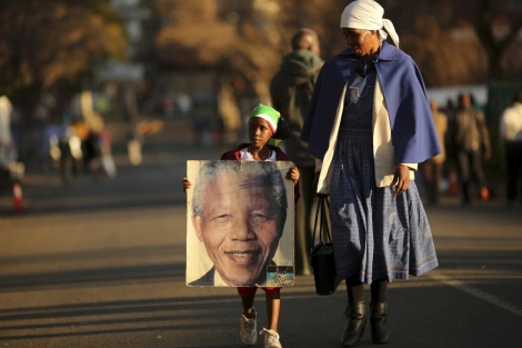 Una nia muestra un pster de Nelson Mandela mientras camina con su madre. | Afp