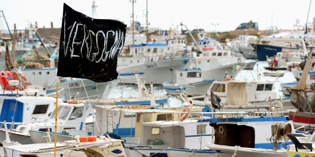 Una bandera negra en la que puede leerse 'Vergenza' ondea en el puerto de Lampedusa. | Afp