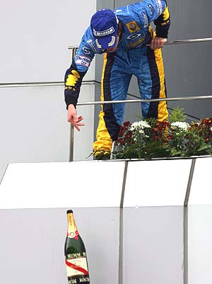 Alonso lanza la botella de la celebración a sus mecánicos. (Foto: EFE)
