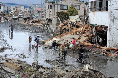Varias personas atraviesan una devastada calle de la ciudad de Miyagi tras en tsunami. | JHK | AD