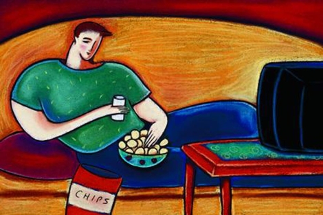 Un joven con exceso de peso, tumbado ante el televisor, mientras come patatas. | El Mundo