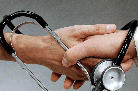 Una mano de un paciente entrelazada por un fonendoscopio de un mdico. | El Mundo