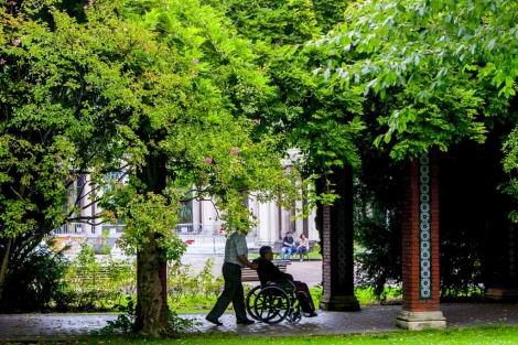 Una persona pasea por un parque de Bilbao empujando a otra en silla de ruedas. | Iaki Andres