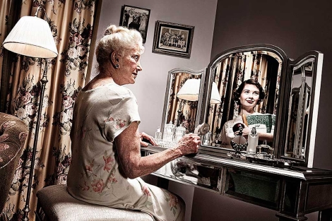 Una anciana se refleja en un espejo, donde puede verse una reproduccin de cmo sera ella de joven