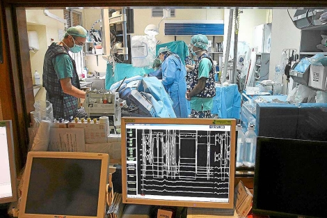 Varios cirujanos en un quirfano vistos a travs del cristal del control