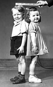 Imagen en blanco y negro de un niño y una niña que estan siendo medidos