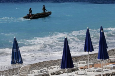 Tumbonas vacías en una playa de Niza mientras soldados armados patrullan desde el mar.
