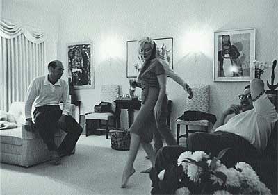 Falsas apariencias. Descalza, copa de champán en mano y con el famoso vestido fucsia de Emilio Pucci, una aparentemente alegre Marilyn baila en el salón de la casa de Henry Weinstein ante la divertida mirada del anfitrión (a la dcha., sentado en el sofá) y algunos invitados.